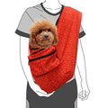 Red pet sling holding a small brown dog with a person wearing a gray shirt and black pants.